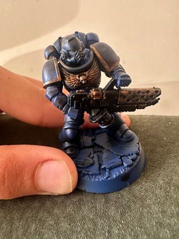 A Space Marine in dark blue armour with gold trim, pyreblaster ready, the first miniature the eldest painted, at the local Warhammer store.